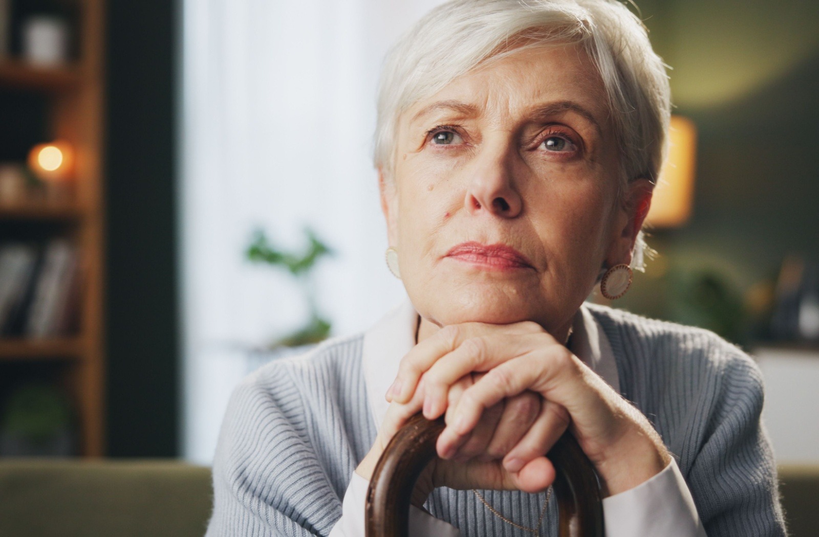 A senior living with dementia sits with their chin resting on their hands while looking off in the distance.
