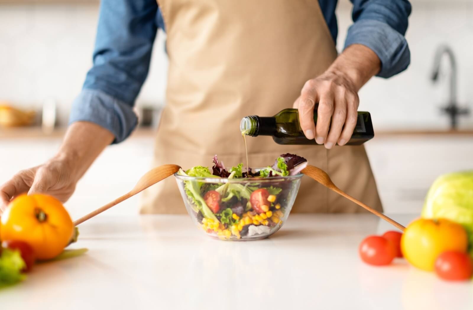 A chef pours a splash of olive oil onto a healthy salad made up of greens, tomatoes, corn, and other healthy veggies.
