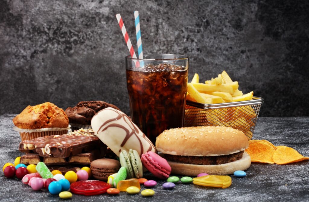 A selection of unhealthy junk food items, including candy, soda, fries, chips, a burger, donuts, and cakes.